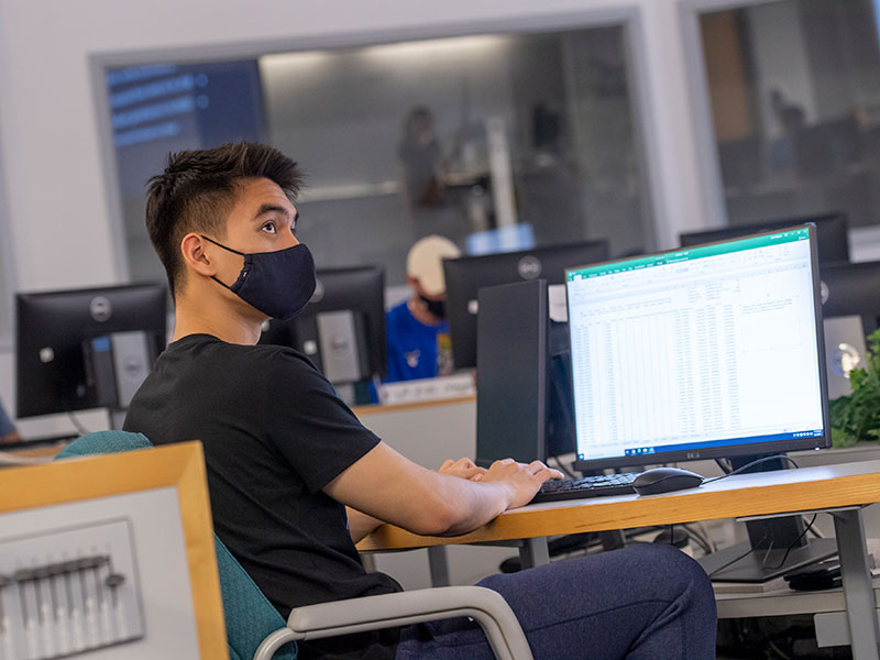 student wearing a mask sits at a computer in a classroom