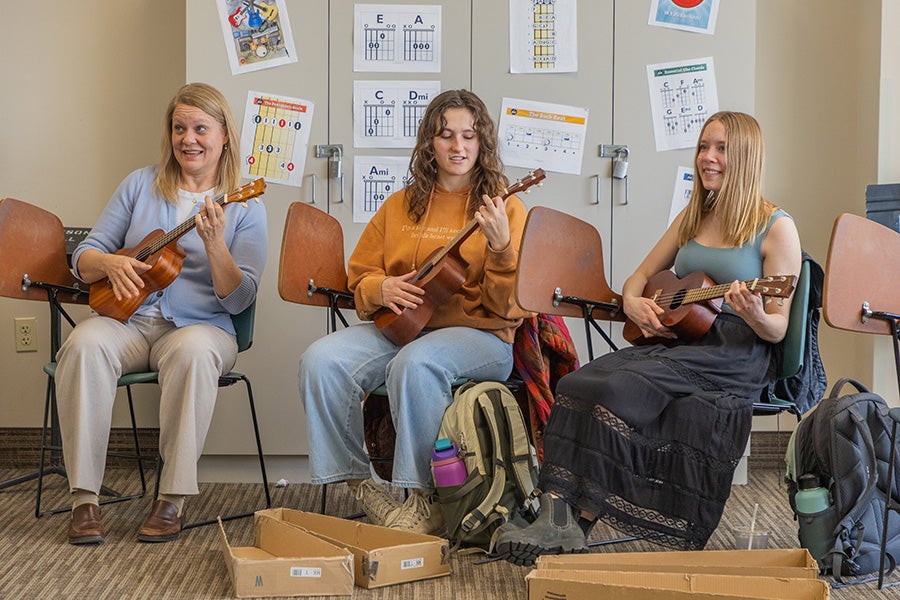 One professor and two students sit in a classroom, strumming ukuleles.