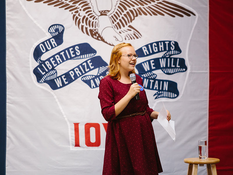 a student giving a speech in front of a large flag