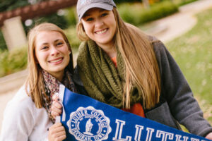 two students holding a Luther College pennant