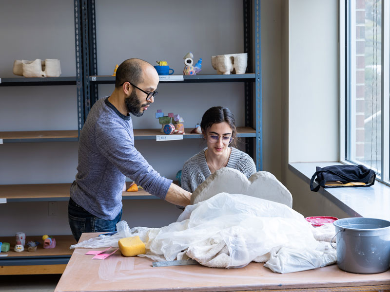 A male professor and female student in the clay studio engage in a critique