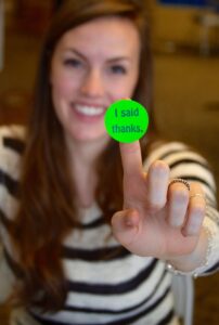 a smiling Luther College student with an "I said thanks" sticker on the end of her finger