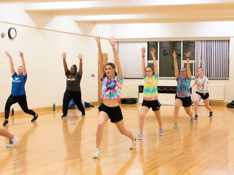 A group of students participate in a yoga class in a studio a window and hardwood floor