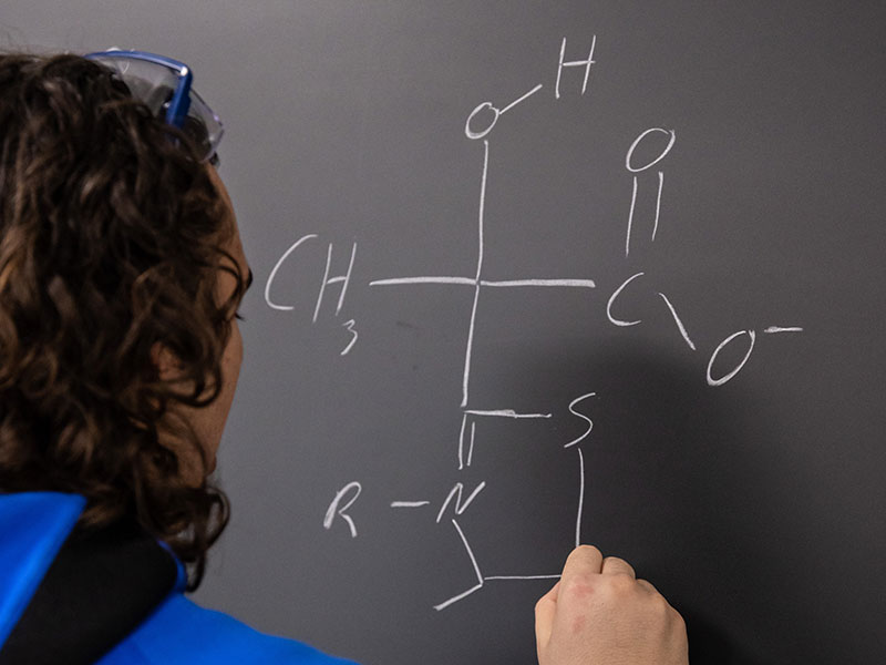 a person writing a chemical molecule structure on a chalk board