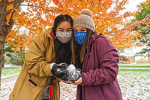 two Luther College students on campus below colorful trees with fall colors