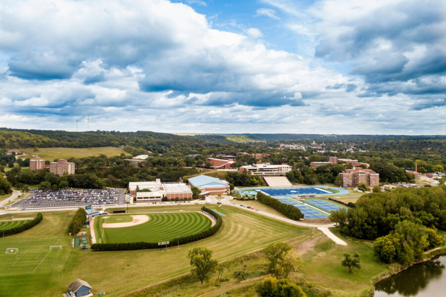 Aerial summer time photo with river in the foreground, athletic fields and academic buildings in the middle ground, and and city of Decorah in the distance.
