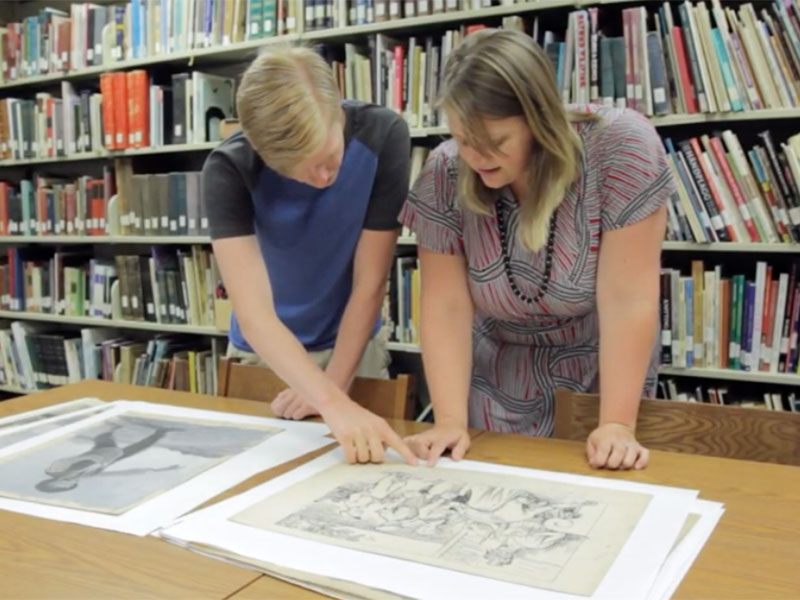 A male student and a female professor lean on a table, looking at documents