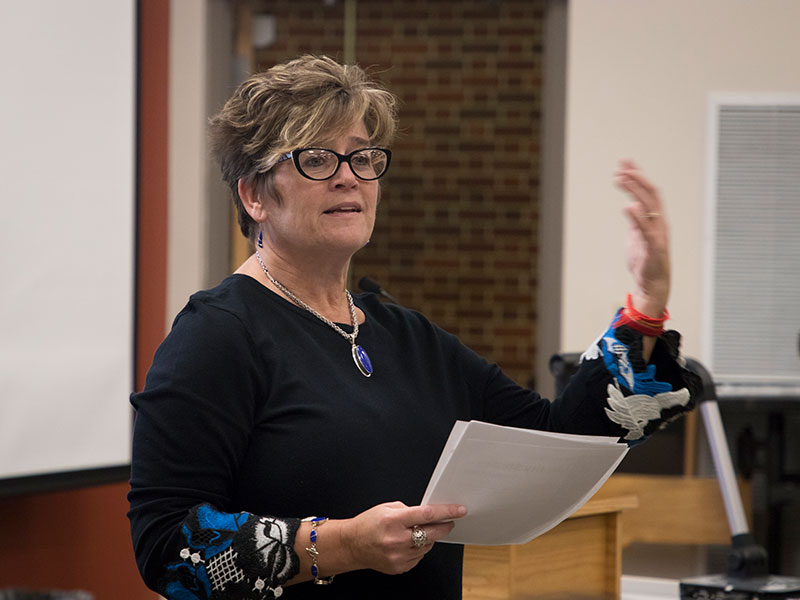 female professor, standing, gesturing with one hand