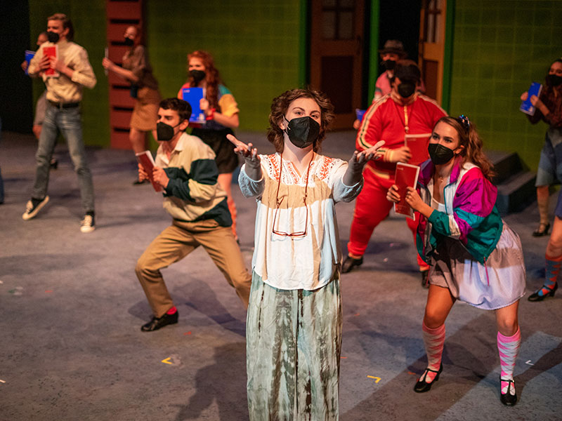 actors singing and dancing on stage in colorful costumes