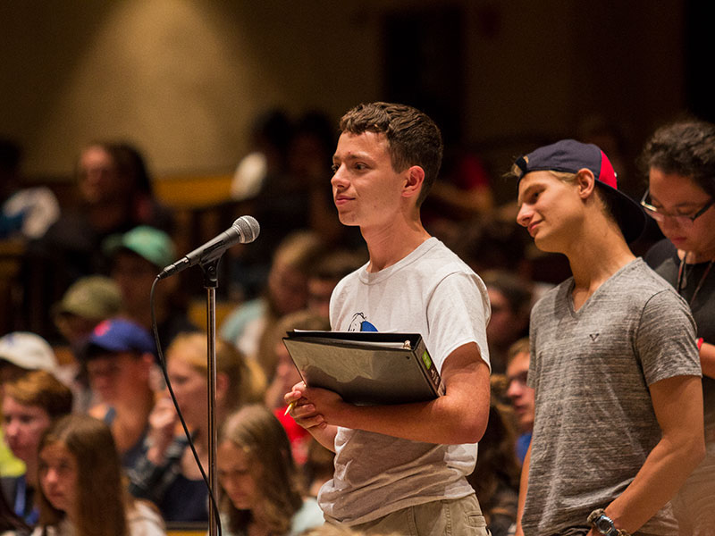 a Luther student holding a binder while standing at a microphone in a lecture hall