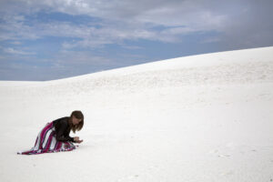 woman on knees in white sand with blue sky