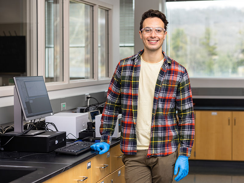 man dressed in plaid shirt stands in a chemistry lab.