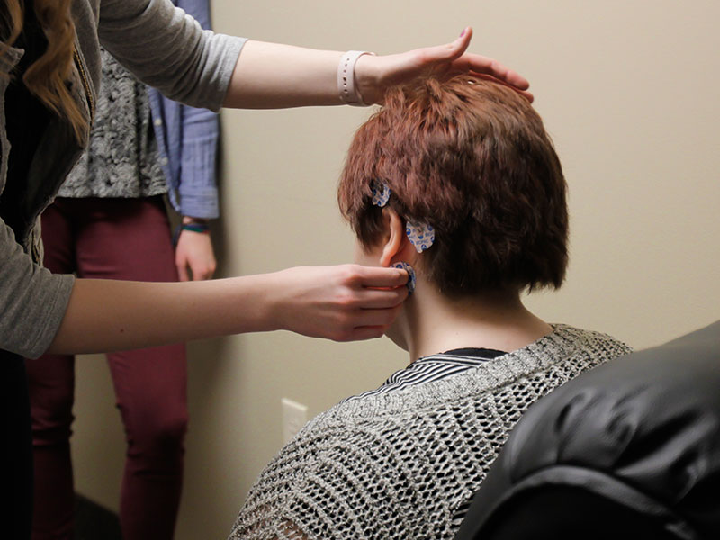 seated person seen from behind, another person is applying sensors to the seated person's head