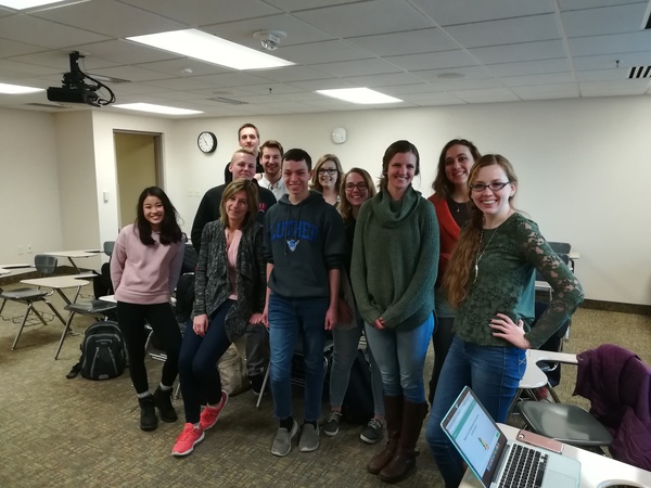 Eleven people stand together in a classroom. 