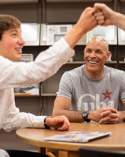 a Luther faculty member smiling while two students fist bump in celebration