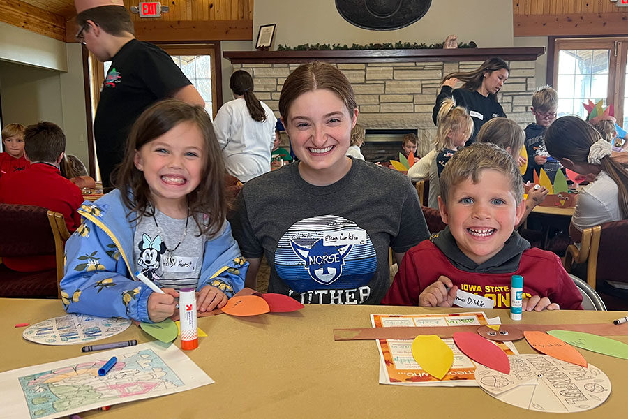 A Luther students PALS volunteer sits between two schoolkids making crafts