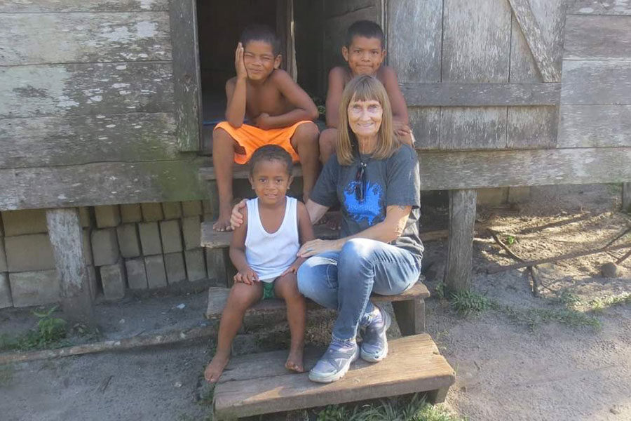 Luther alumna Nola Nackerud sits on house steps with three smiling young kids
