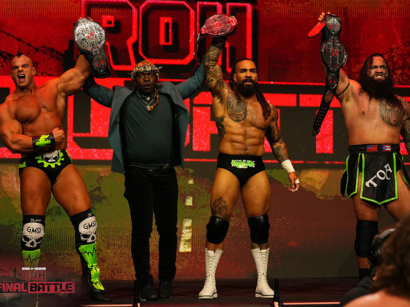 Photo of Jasper Kange with teammates, their arms raised in victory, holding championship belts