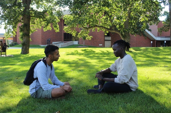Two students sitting on the grass together on a sunny day. 