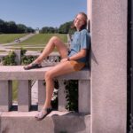 Berit sits on a monument with paths and green grass in the background