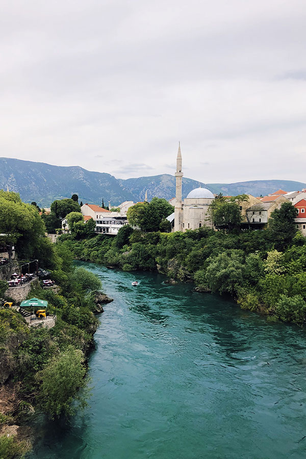 A waterway with trees and buildings on either side and a mountain range in the distance