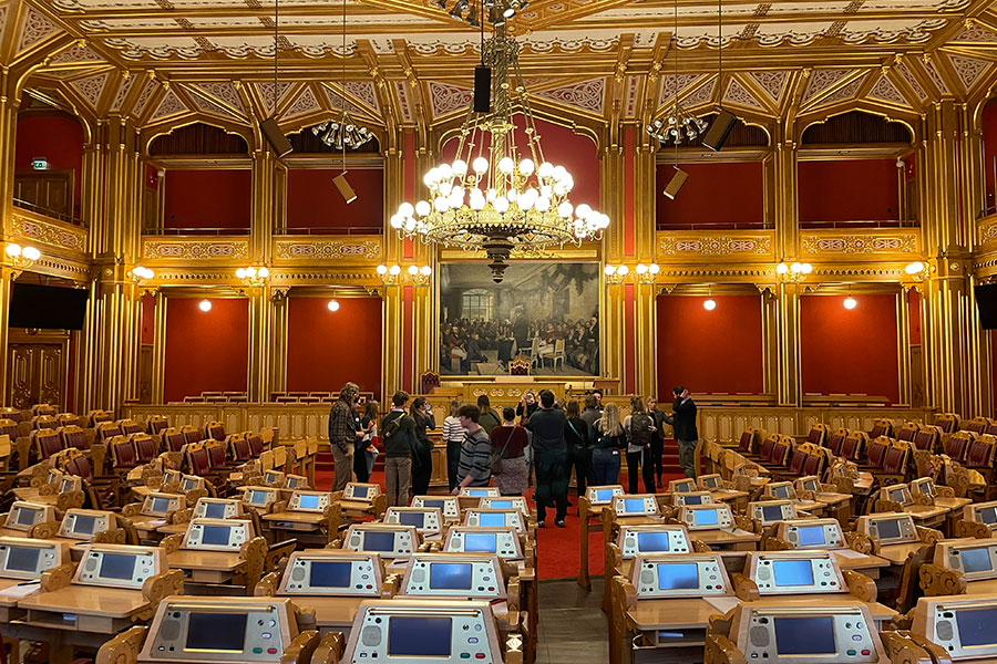 A group of people conversing in ornate two-story interior with chandelier, seats, and desks with monitors