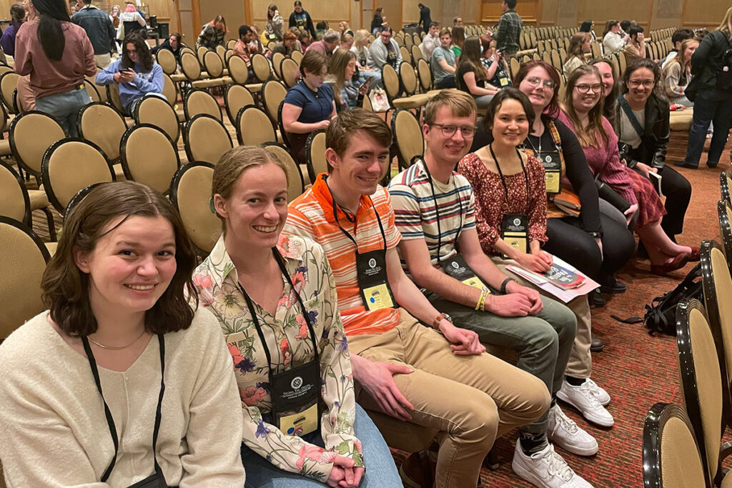 Students sit in a row, smiling at the camera.