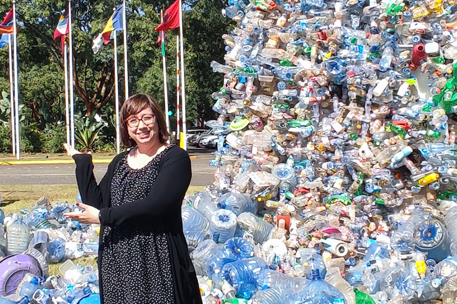 A woman standing in front of a line of flags and a sculpture made frmo plasitc bottles