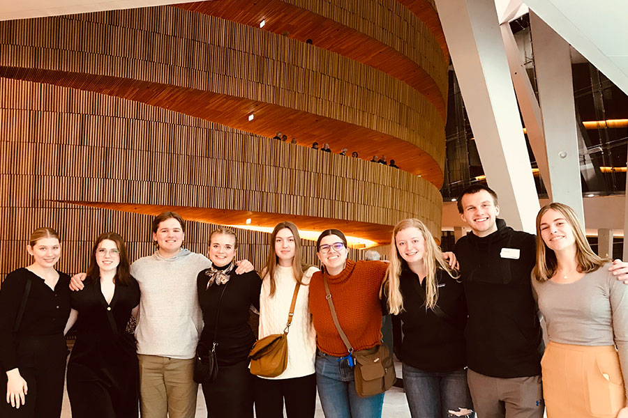 Nine people standing in a line in a large building