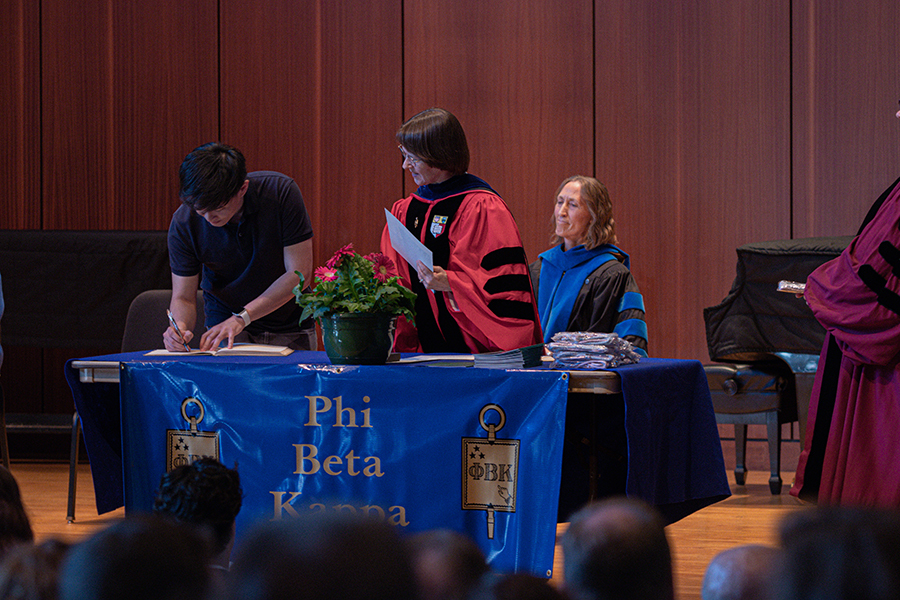 A student leans over a table. Tablecloth on the table says Phi Beta Kappa and shows the golden key of Phi Beta Kappa.