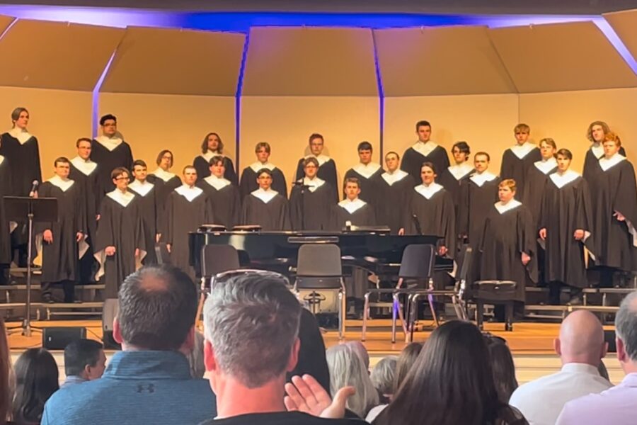 The choir on stage, dressed in black robes with white collars.