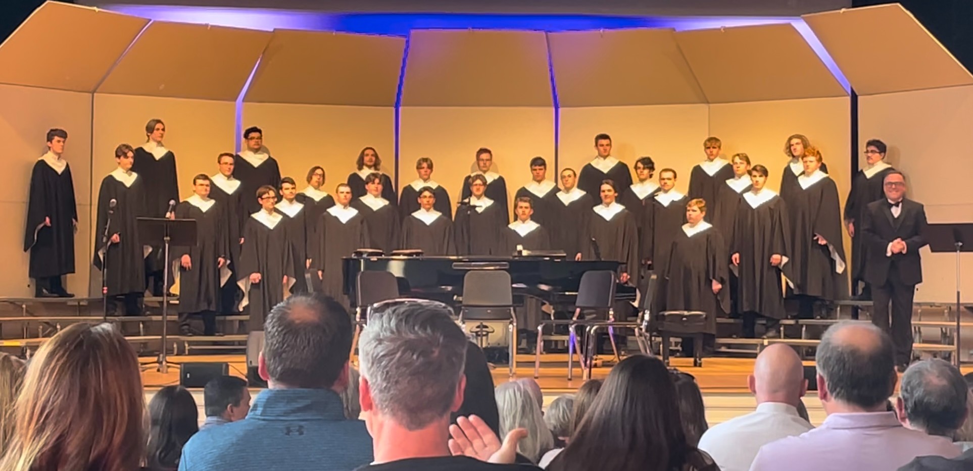 The choir on stage, dressed in black robes with white collars.