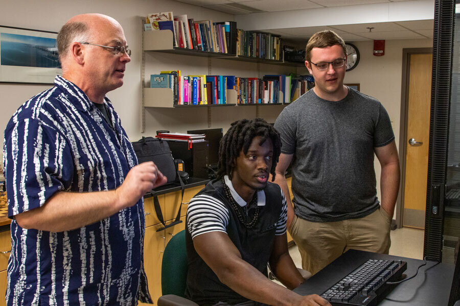 Professor Pedlar stands next to two students, consulting with them over a computer