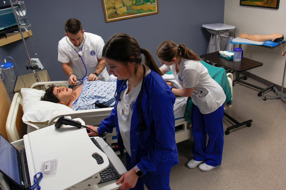 Three students practice medicine on a fake patient during simulation