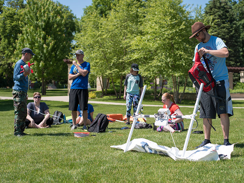 A group of people sitting and standing on a green lawn with various pieces of equipment