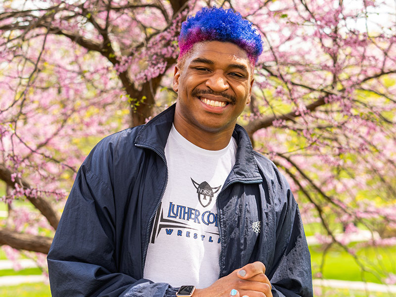 A man with smiling in front of a tree with pink blossoms