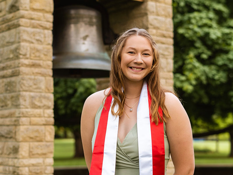 A woman wearing a colored stole standing in front of the Luther Bell