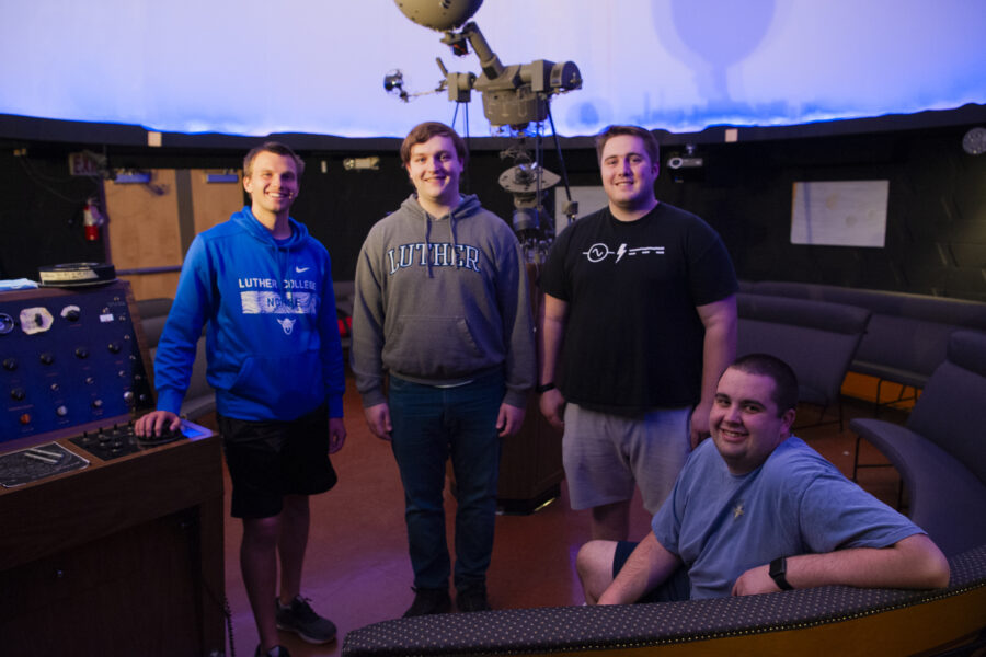 Three standing and one seated student near a console in a planetarium