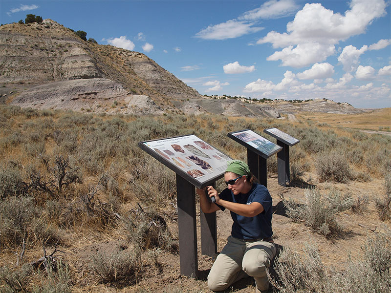 A woman installing public signage near a rock formation in desert scrub-land