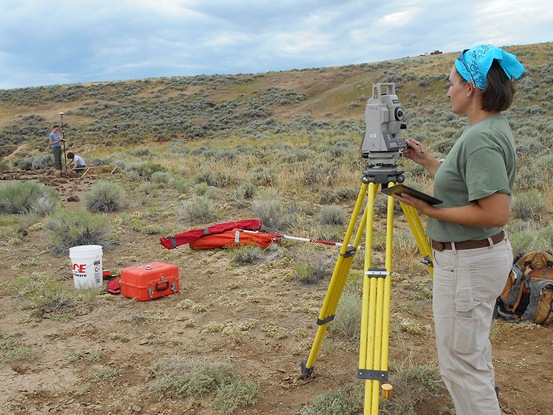 A woman in a desert scrub-land using surveying equipment