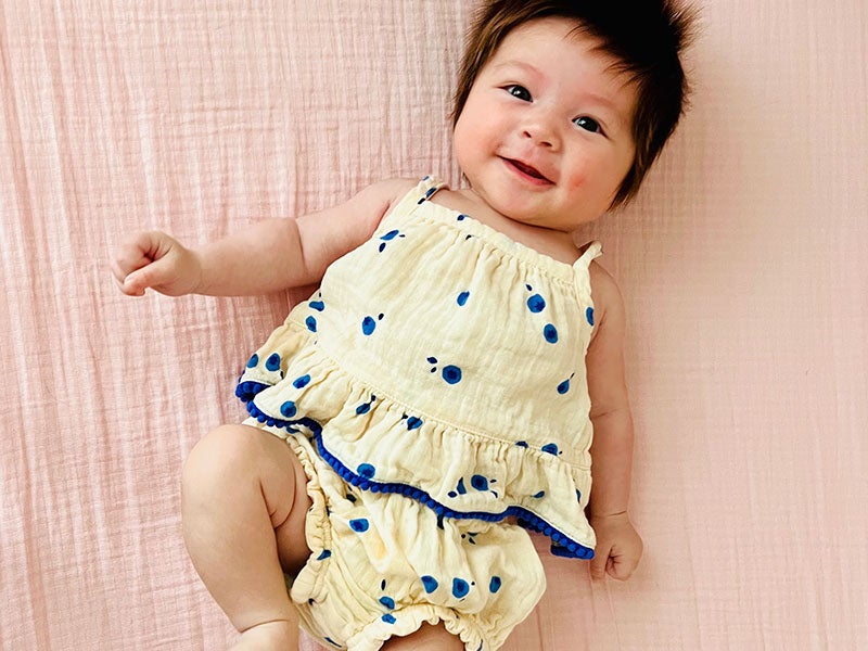 A baby in a yellow jumpsuit lying on a pink blanket