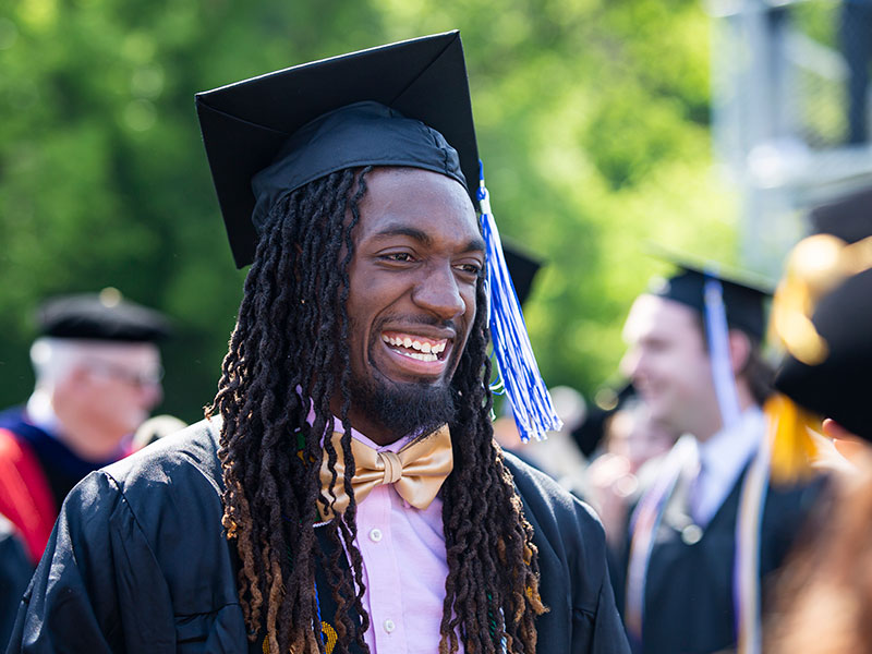 A smiling man from the chest up wearing a graduation cap and gown