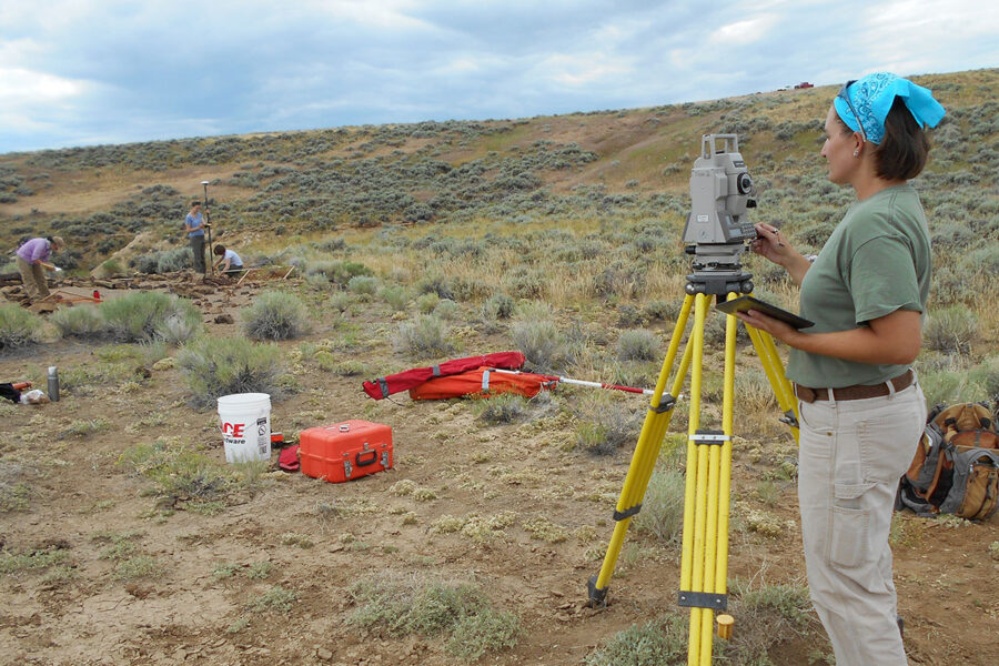 A woman in a desert scrub-land using surveying equipment