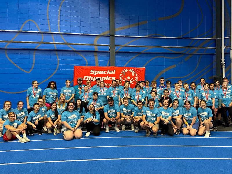 A large group of people in matching turquoise t-shirts in front of a Special Olympics banner