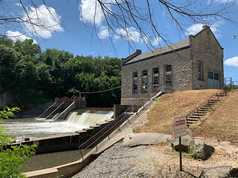 A historic brick building next to a river with a low-head dam spanning the river