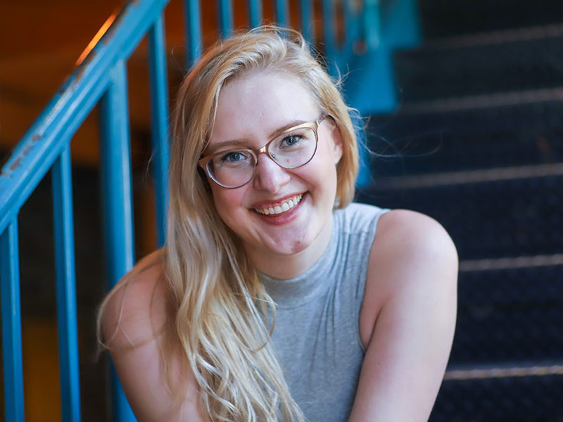 A woman sitting on stairs with an aqua railing, smiling at the camera