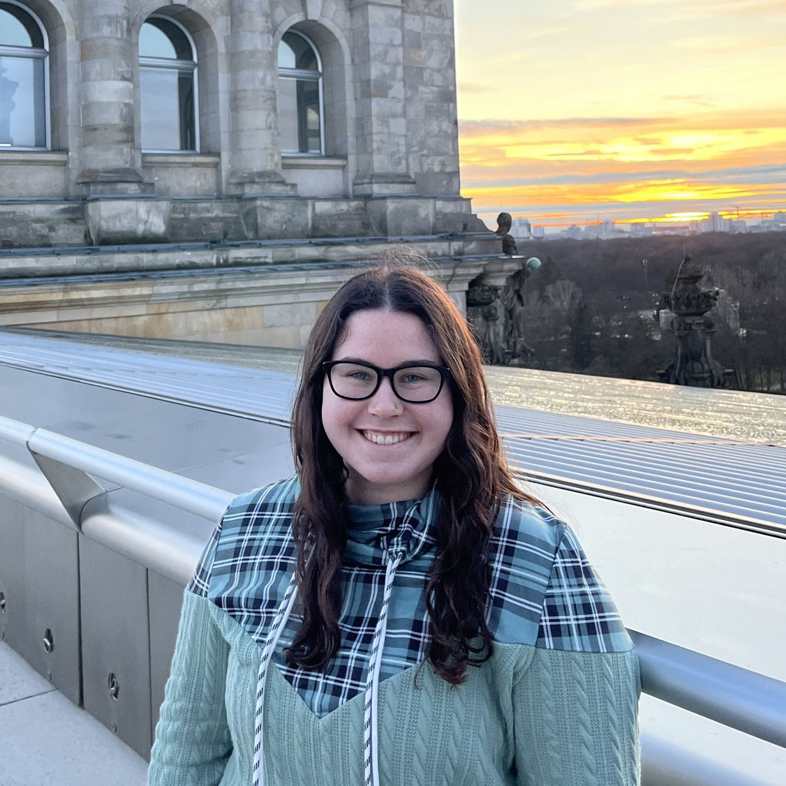 Jessi smiles at the camera, with a beautiful building and sunset in the background.