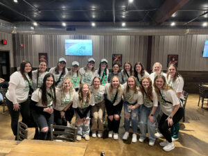 Members of Alpha Beta Psi take group photo in matching white shirts with green bead necklace