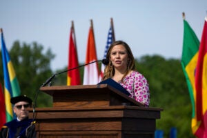 Mallory Heinzeroth stands at a podium outside in a pink floral print dress.