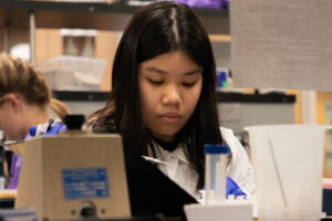 Young woman in a white lab coat looking at samples in a lab. 